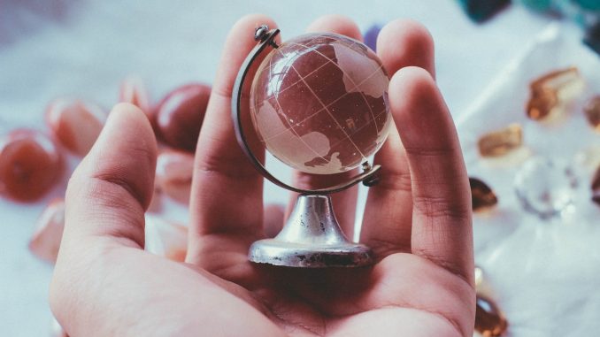 person holding gray metal framed desk globe paper weight